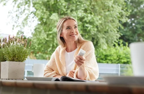 Frau bedient Funk-Steuerelement für Sonnenschutz am Fenster